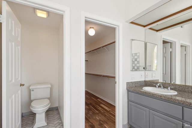 bathroom featuring vanity, a walk in closet, toilet, and baseboards