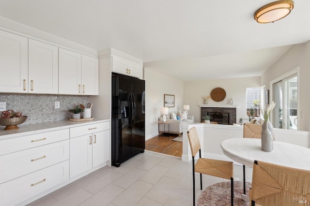 kitchen with tasteful backsplash, light countertops, black fridge, a fireplace, and white cabinets