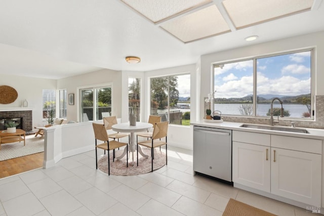 kitchen with a water view, a sink, a fireplace, light countertops, and dishwasher