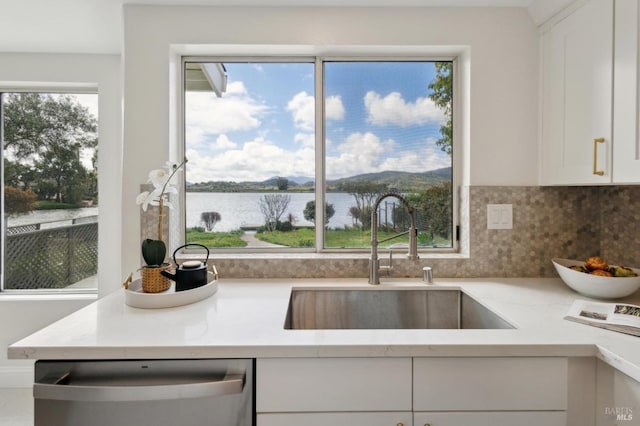 kitchen featuring a sink, light countertops, white cabinets, a water view, and dishwasher