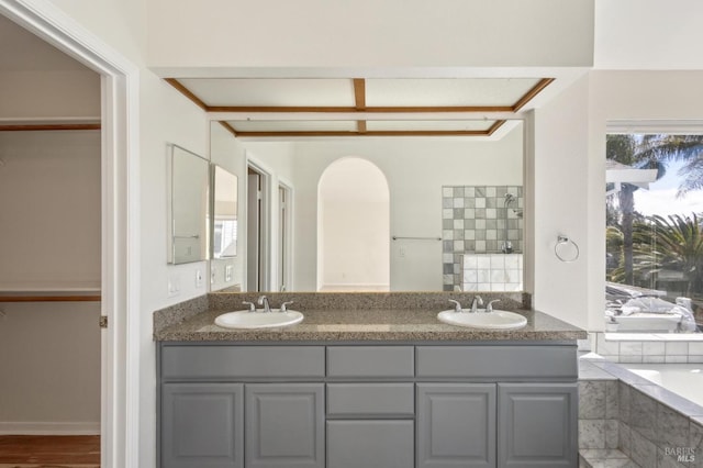 full bathroom with double vanity, a garden tub, and a sink