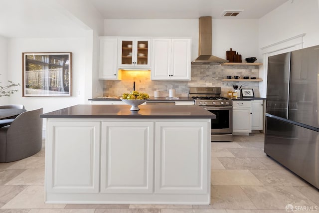 kitchen featuring a kitchen island, white cabinets, backsplash, stainless steel appliances, and wall chimney exhaust hood