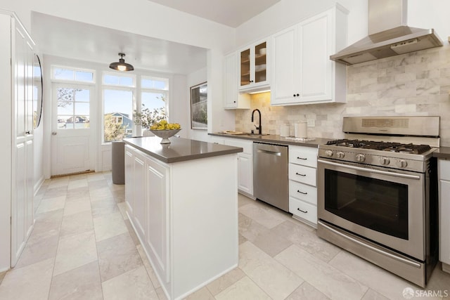 kitchen featuring wall chimney range hood, a kitchen island, stainless steel appliances, decorative backsplash, and white cabinets