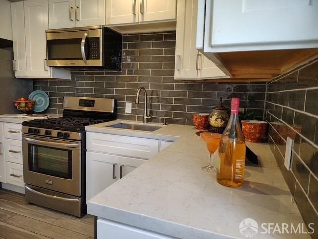 kitchen with backsplash, light stone counters, white cabinets, stainless steel appliances, and a sink