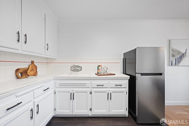 kitchen with white cabinetry, tasteful backsplash, ornamental molding, and stainless steel refrigerator