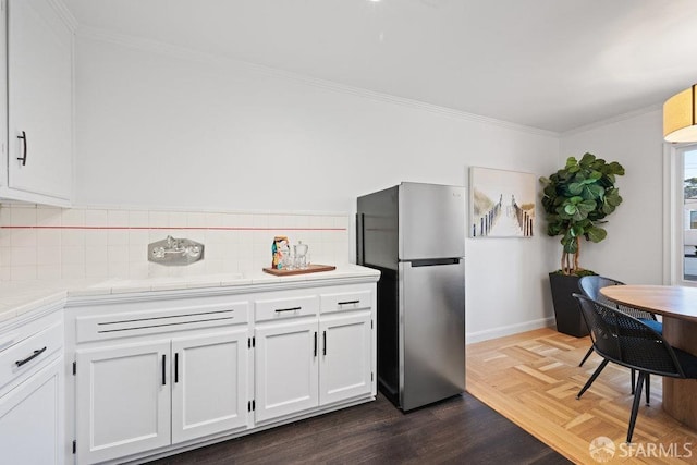 kitchen featuring stainless steel refrigerator, ornamental molding, dark parquet floors, white cabinets, and backsplash