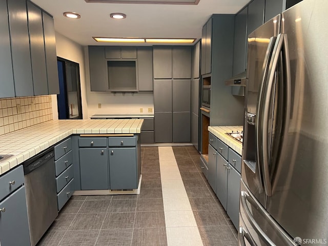 kitchen featuring stainless steel appliances, gray cabinets, tile counters, and dark tile patterned floors