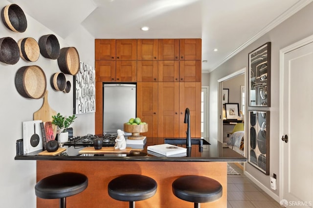 kitchen featuring dark countertops, a breakfast bar area, tile patterned floors, fridge, and a sink