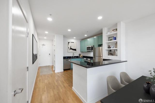 kitchen with light hardwood / wood-style floors, sink, kitchen peninsula, green cabinets, and appliances with stainless steel finishes