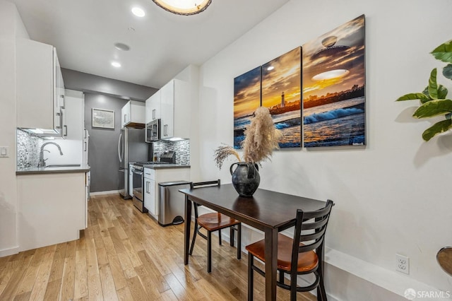 kitchen with a sink, appliances with stainless steel finishes, backsplash, light wood finished floors, and dark countertops