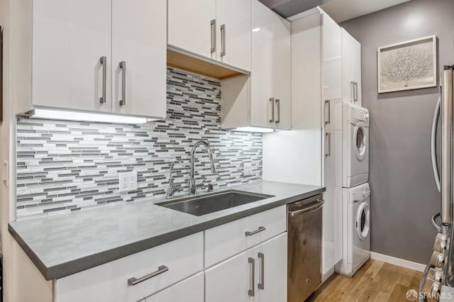 kitchen with stainless steel appliances, stacked washer / drying machine, tasteful backsplash, white cabinets, and a sink