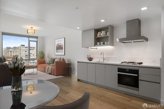 1545 Pine St Unit 802, San Francisco, CA 94109 - kitchen featuring stainless steel oven, wall chimney range hood, gas stovetop, light wood-style floors, and gray cabinetry