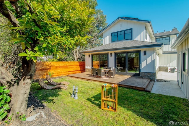 rear view of house featuring fence, roof with shingles, a yard, a deck, and board and batten siding