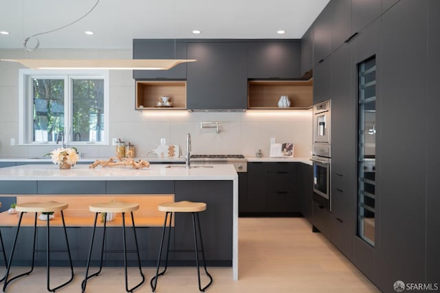 kitchen with a kitchen bar, light countertops, stainless steel oven, modern cabinets, and open shelves