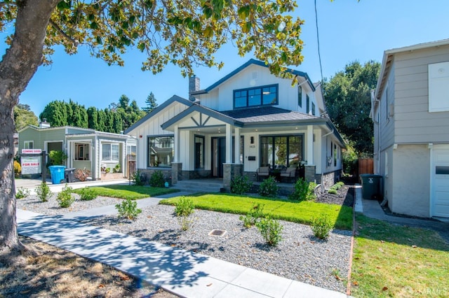 modern farmhouse with a front lawn, board and batten siding, covered porch, and a chimney