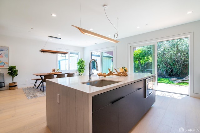 kitchen with modern cabinets, an island with sink, light wood-style floors, and a sink