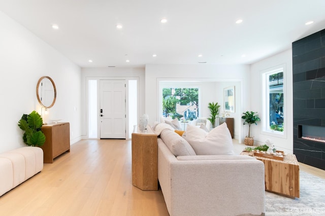 living room with recessed lighting, a large fireplace, and light wood-style flooring