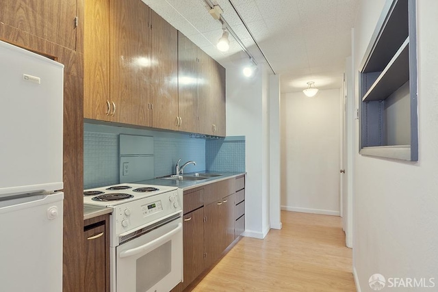 kitchen featuring white appliances, a sink, backsplash, light wood-type flooring, and rail lighting