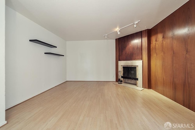 unfurnished living room featuring track lighting, light wood-style floors, and a fireplace with raised hearth