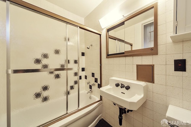 bathroom with tile walls, enclosed tub / shower combo, a sink, and toilet