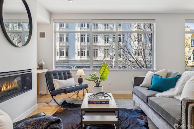 living room featuring a glass covered fireplace, visible vents, baseboards, and wood finished floors