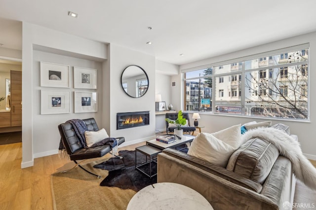 living area with a glass covered fireplace, light wood-style flooring, baseboards, and recessed lighting