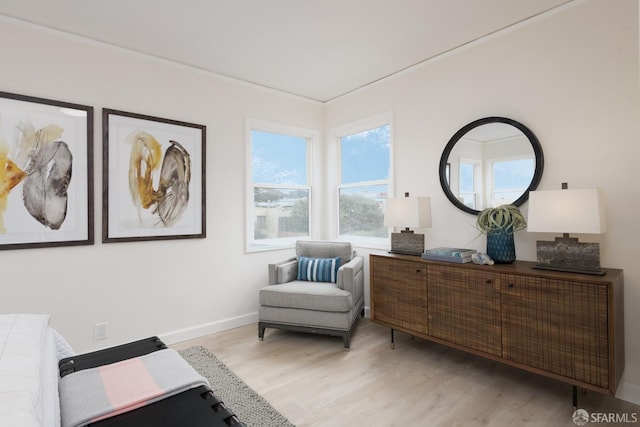 sitting room featuring crown molding, light wood-style flooring, and baseboards