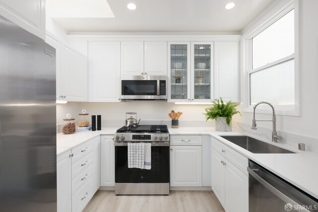 kitchen with stainless steel appliances, light countertops, white cabinets, and a sink