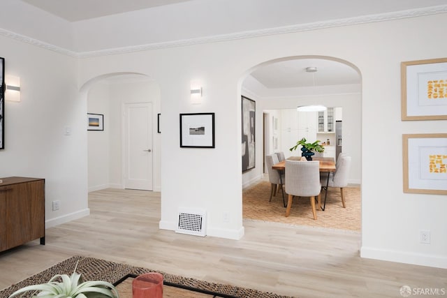 corridor with light wood finished floors, baseboards, visible vents, and arched walkways