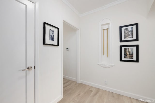 hall with light wood finished floors, ornamental molding, and baseboards