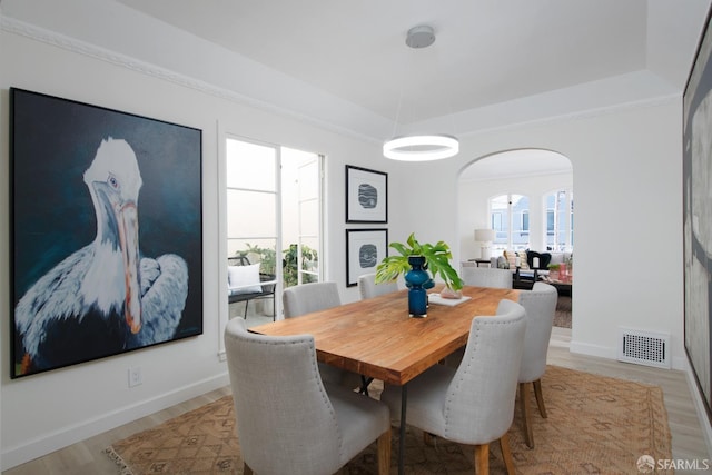 dining room with baseboards, visible vents, arched walkways, light wood-style flooring, and a tray ceiling