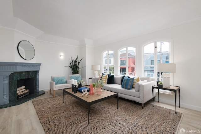 living area featuring light wood-type flooring, a premium fireplace, baseboards, and crown molding