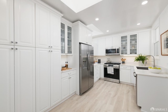 kitchen with recessed lighting, a sink, white cabinets, appliances with stainless steel finishes, and light wood-type flooring