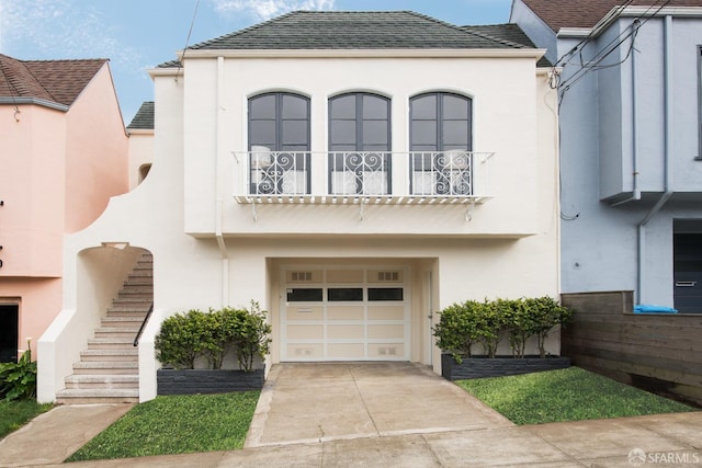 view of front of home featuring stucco siding, stairway, an attached garage, a balcony, and driveway