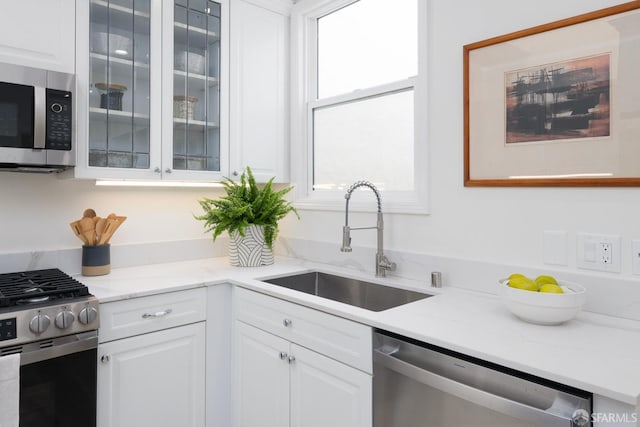 kitchen featuring appliances with stainless steel finishes, glass insert cabinets, white cabinets, a sink, and light stone countertops