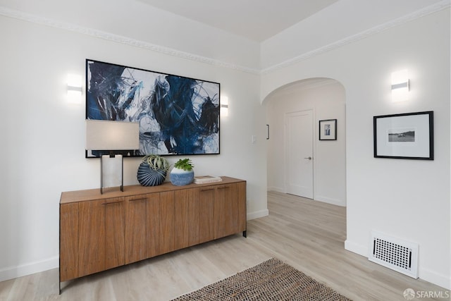 hall featuring arched walkways, baseboards, visible vents, and light wood finished floors