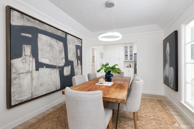 dining space featuring a raised ceiling, light wood-style flooring, and baseboards