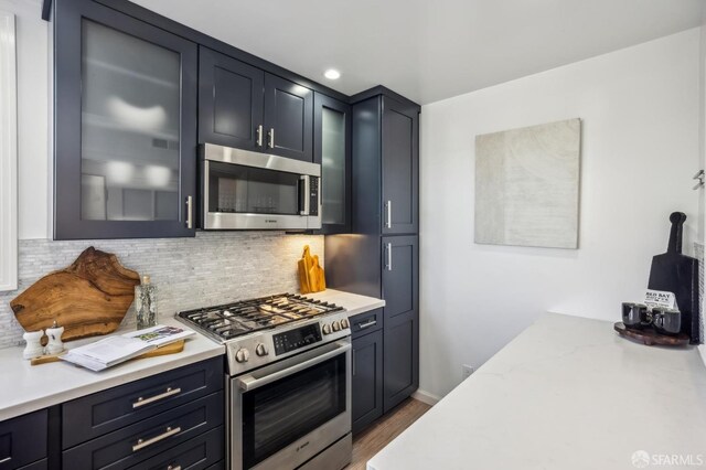 kitchen with tasteful backsplash, appliances with stainless steel finishes, dark hardwood / wood-style floors, and light stone countertops