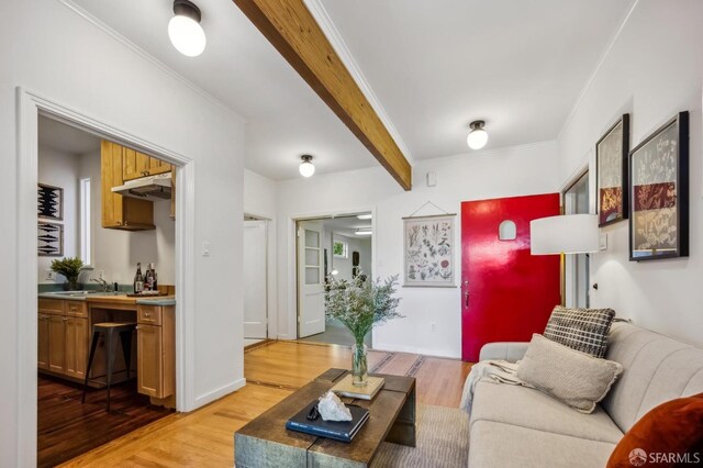 living room with beamed ceiling, crown molding, sink, and light wood-type flooring