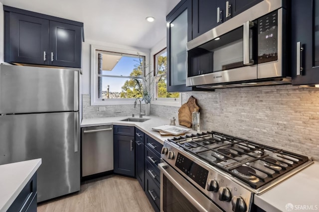 kitchen featuring blue cabinets, sink, appliances with stainless steel finishes, light hardwood / wood-style floors, and decorative backsplash