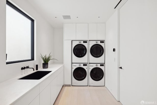 clothes washing area featuring sink, cabinets, light wood-type flooring, stacked washing maching and dryer, and washing machine and dryer