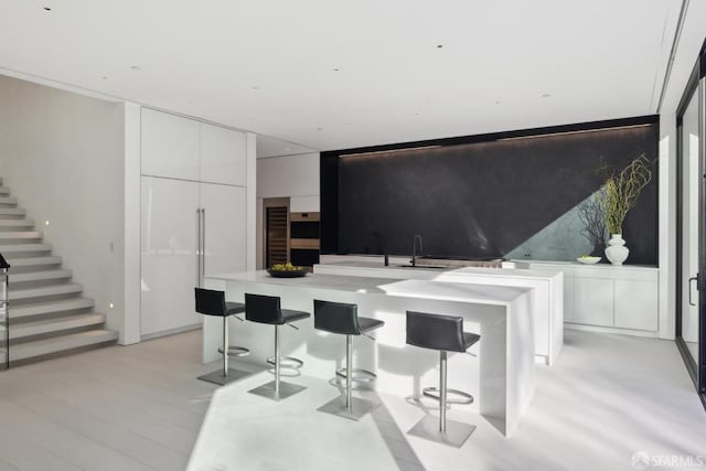 kitchen with sink, a kitchen breakfast bar, a center island, light hardwood / wood-style floors, and white cabinets