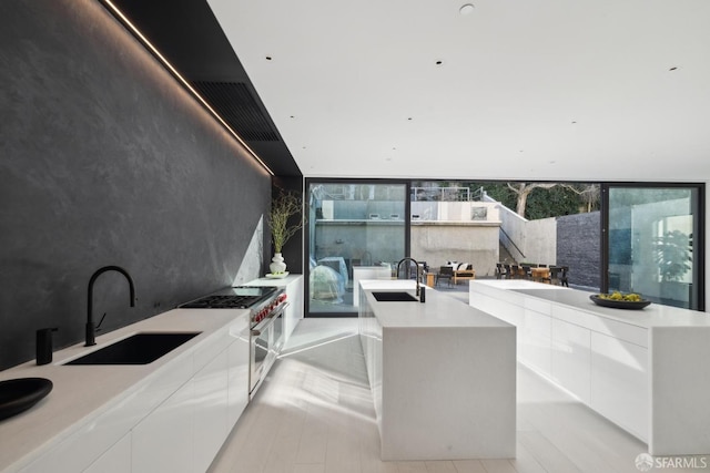 interior space featuring white cabinetry, double oven range, a kitchen island with sink, and sink