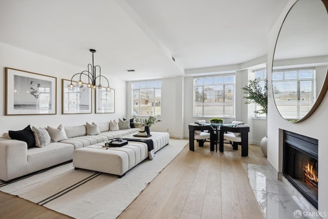 living area with a fireplace with flush hearth, light wood-style flooring, baseboards, and a chandelier