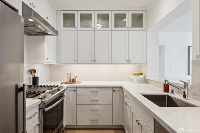 kitchen featuring light stone counters, a sink, decorative backsplash, appliances with stainless steel finishes, and under cabinet range hood