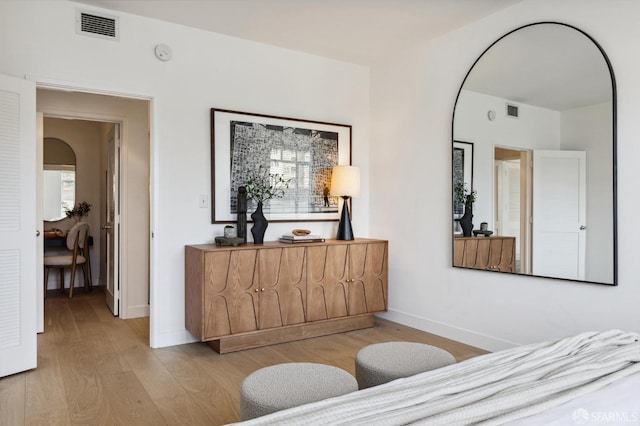bedroom with arched walkways, light wood-style floors, visible vents, and baseboards