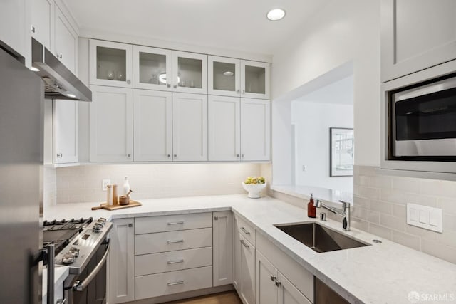 kitchen with stainless steel appliances, a sink, backsplash, light stone countertops, and under cabinet range hood