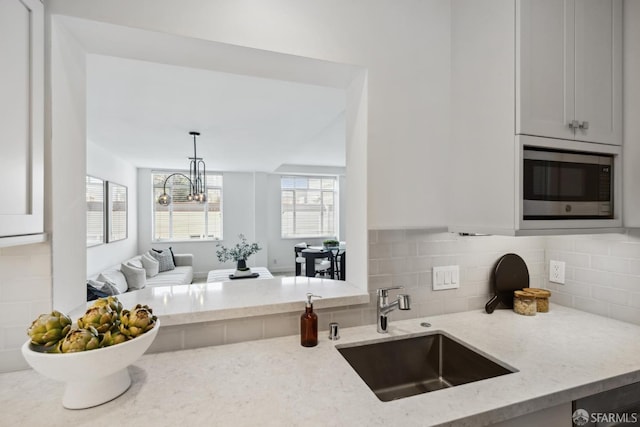 kitchen featuring stainless steel microwave, tasteful backsplash, light stone countertops, and a sink
