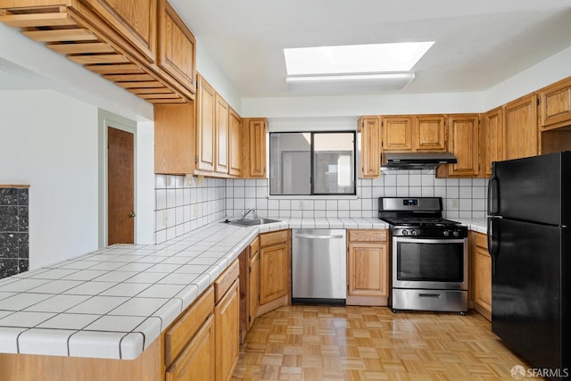 kitchen with tile counters, stainless steel appliances, backsplash, sink, and light parquet flooring