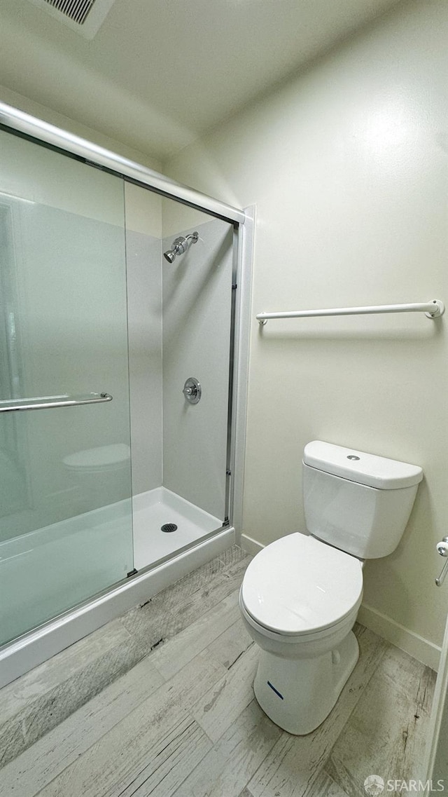 bathroom featuring a shower with shower door, hardwood / wood-style flooring, and toilet